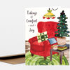 A folded greeting card with the text "Tidings of Comfort and Joy" and a watercolor illustration of a red armchair with pillows, a lit Christmas tree, a small table, and a hanging lamp.