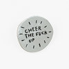 A round silver lapel pin with black hand-drawn text that reads "CHEER THE FUCK UP" and small radiating mark accents around the edge.