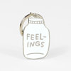 A silver-toned keychain charm shaped like a jar with the word “FEEL-INGS” cut out across the front.