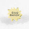 A gold-tone starburst pin with the words "GOOD ENOUGH" embossed in black lettering.