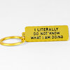 A gold rectangular keychain tag with black embossed text reading "I LITERALLY DO NOT KNOW WHAT I AM DOING" attached to a split key ring.
