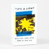A white card deck box with a central yellow starburst graphic framed by blue tape-like strips and handwritten text that reads "IT'S A SIGN," "INTUITIVE CARD DECK," and "ADAM JK (AND YOU)".