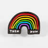 A black rainbow lapel pin shaped like an arch with rainbow stripes and the words "THEN" and "NOW" in white.