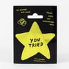 A pale yellow star-shaped sticker on black backing with the words "YOU TRIED" in black, plus small text reading "An attempt was made," "Please enjoy this acknowledgement," and "It's a sticker."