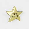 A gold star-shaped enamel pin with the words "YOU TRIED" in black lettering.