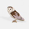 A barn owl enamel pin with a gold-tone outline, white face and body, brown wings, and pale pink accents, shown perched on one foot.