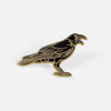 A black and gold enamel pin shaped like a crow standing in profile with its beak open.