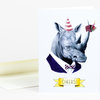 A folded greeting card featuring an illustrated rhinoceros wearing a striped party hat, tuxedo, and bow tie, holding a small cupcake with a candle, with the word "CHEERS!" on a yellow banner.