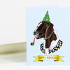 A folded birthday greeting card featuring an illustrated goat wearing a green party hat, a floral collar, and a ribbon banner that says "HAPPY BIRTHDAY!"