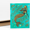 A folded birthday greeting card with a turquoise cover showing a black-and-gold mermaid illustration and the text "HOPE YOUR BIRTHDAY IS AS MAGICAL AS YOU ARE".