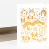 A folded greeting card with a gold illustration of multiple dog faces around a ribbon banner reading "BITCHES UNITE".