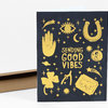 A black greeting card with yellow illustrations and the text "SENDING GOOD VIBES," featuring a hand, eye, horseshoe, moon, clover, shooting stars, and a ticket-like shape labeled "GOLDEN TICKET."