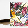 A folded greeting card with a colorful hand-drawn spread of fruits, cheese, olives, salami, and herbs, and the text "HAPPY BIRTHDAY, LET'S EAT!" on the front.