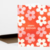A folded greeting card with a bold orange background covered in pink and white flower shapes and the text "HAPPY BIRTHDAY" on the front.