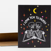 A black greeting card with the text "I LOVE YOU TO DEATH" above two white skeletons, a yellow crescent moon, and colorful star-like symbols.