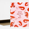 A folded greeting card with a pink front covered in red shrimp illustrations and the text "YOU'RE SHRIMPLY THE BEST" in the center.