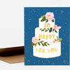 A folded greeting card with a three-tier white cake illustration decorated with pink flowers and green leaves, and the words "SO HAPPY FOR YOU" in gold lettering.