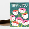 A folded greeting card with the words “THANK YOU” in white hand-drawn lettering above a pattern of pink, orange, and white cone flowers with green stems and leaves.