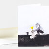 A folded greeting card with a minimalist illustration of a person crouching to plant or transplant a small sprout with two bright yellow leaves into a dark cutaway of soil.