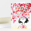 A folded greeting card shows a stylized smiling girl beneath pink flower branches with small bees and an open white envelope behind it.