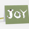 A folded greeting card with an olive green cover printed with the word “JOY” formed by three illustrated people in white clothing doing yoga poses.