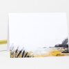 A folded greeting card with a minimalist landscape illustration featuring pale sky, black brushy grasses, and yellow and gray shoreline accents along the bottom edge.