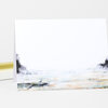 A folded greeting card with a minimalist coastal landscape illustration in pale gray, blue, and sand tones and no visible text.