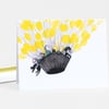 A folded notecard featuring an illustration of a dark basket-like balloon gondola carrying small figures and cats beneath many bright yellow balloons.