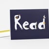 A dark navy notecard with the word "Read" spelled in large white illustrated letters made from people and a bird.
