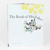 A hardcover book titled “The Book of Mistakes” by Corinna Luyken with a white cover, yellow balloons at the top, and a small illustration of several people clustered together below the title.