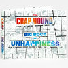 A hardcover book titled “THE CRAP HOUND BIG BOOK OF UNHAPPINESS” with a multicolor gradient title and a black-and-white comic-style cover collage of expressive faces and small illustrated scenes.
