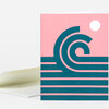 A folded greeting card with a pink cover featuring a teal stylized wave design and a small white circle in the upper right, with the inside blank white.
