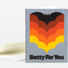 A folded greeting card with a large stylized bat graphic in black, red, orange, and yellow and the words “Batty For You” printed in bold black text on the front.