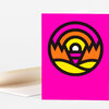 A folded greeting card with a bright pink front featuring a bold black circular sunrise-and-landscape graphic in orange, yellow, and magenta.