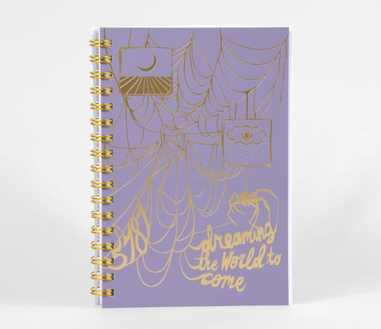 A lavender planner or notebook cover with metallic yellow spiderweb line art, two hanging moon-themed squares, a small spider illustration, and the text "dreaming the World to come."