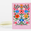 A pink greeting card with a colorful floral folk-art design and the words “HAPPY BIRTHDAY” printed at the bottom, shown with a white envelope.