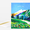 A folded greeting card with the words “THANK YOU” above a colorful mountain landscape and a meadow of flowers on the front.