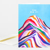 A greeting card with a blue front featuring the white text "YOU DID IT!" above a colorful abstract striped mountain design, shown with a white envelope.