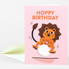 A pink greeting card with the text "HOPPY BIRTHDAY" and an illustration of a smiling lion bouncing on a white ball.