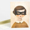 A folded greeting card with an illustrated girl wearing a black bandit mask, short brown hair, a white collar, and a brown sweater with stitched details.
