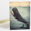 A folded greeting card with an illustration of a large whale rising from the sea near a sailing ship.