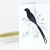 A folded greeting card featuring a black bird with a long tail perched among pale green stems and small white flowers.