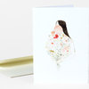 A folded greeting card with a watercolor-style illustration of a faceless woman whose floral bouquet body is made of pastel flowers and stems.