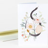 A folded greeting card with a watercolor-style illustration of a black snake coiled among pale flowers and green leaves on the front.