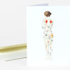 A blank folded greeting card with a watercolor-style illustration of a nude woman seen from behind, covered in a floral garden pattern, with a white envelope.