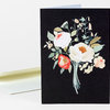 A folded greeting card with a black front featuring a bouquet of white, cream, and red flowers with pale green leaves.
