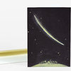 A greeting card with a black cover featuring a yellow-green shooting star, scattered stars, and a row of small figures standing on a curved hill at the bottom.