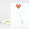 A folded greeting card with a simple illustration of a small girl holding a red heart-shaped balloon on a string.