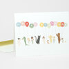 A folded greeting card with an illustration of pastel balloons spelling “HAPPY BIRTHDAY” above a row of small misfit characters, including people and animals.