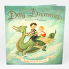 A book cover titled "Day Dreamers" with the subtitle "A Journey of Imagination" and the author name "Emily Winfield Martin," illustrated with two children riding a green dragon in the clouds.